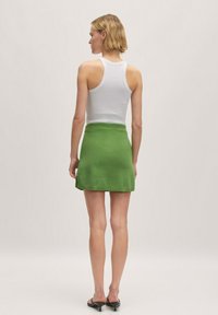 Witte tanktop gecombineerd met een groene gebreide rok. De rok heeft een licht uitlopende vorm met een geribbelde tailleband en een zachte textuur.