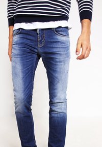 Blå denimjeans med slim fit, med en urtvättad design, fem fickor och sömnadsdetaljer. Bärs med en randig marinblå tröja.