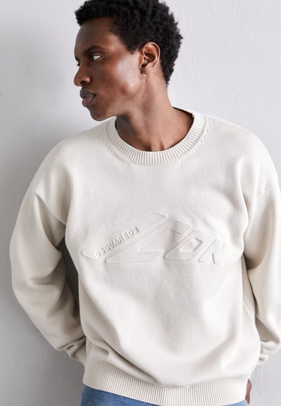 Pull crème clair avec un col et des poignets côtelés. Présente un design de logo surélevé "DSQUARED2" sur le devant. Texture en tricot douce.