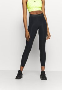 Czarne legginsy z wysokim stanem, z delikatnym logo Nike. Materiał wydaje się gładki i elastyczny, idealny do odzieży sportowej.