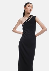 Schwarzes ärmelloses Kleid mit asymmetrischem Ausschnitt, das dekorative Knöpfe an einer Schulter und eine taillierte Silhouette aufweist.