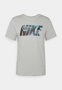 Light gray cotton t-shirt featuring a large, multi-colored Nike logo with a camouflage pattern across the chest. Short sleeves and crew neck.