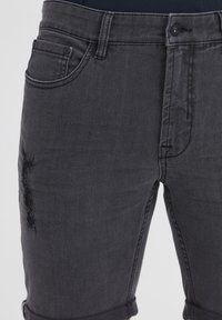 Zwarte denim jeans met een distressed detail op het dijbeen, een klassiek ontwerp met vijf zakken en omgeslagen pijpen. Duurzame stof met een gladde textuur.