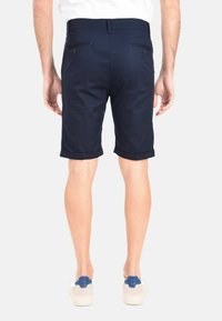 Pantaloni blu navy realizzati in tessuto liscio, con orli arrotolati, due tasche posteriori con bottoni e una vita strutturata.