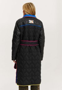 Čierny prešívaný kabát s tvarmi srdca, má modrý golier, ružové a modré akcenty a štítok na zadnej strane. Dlhé rukávy, opasok.