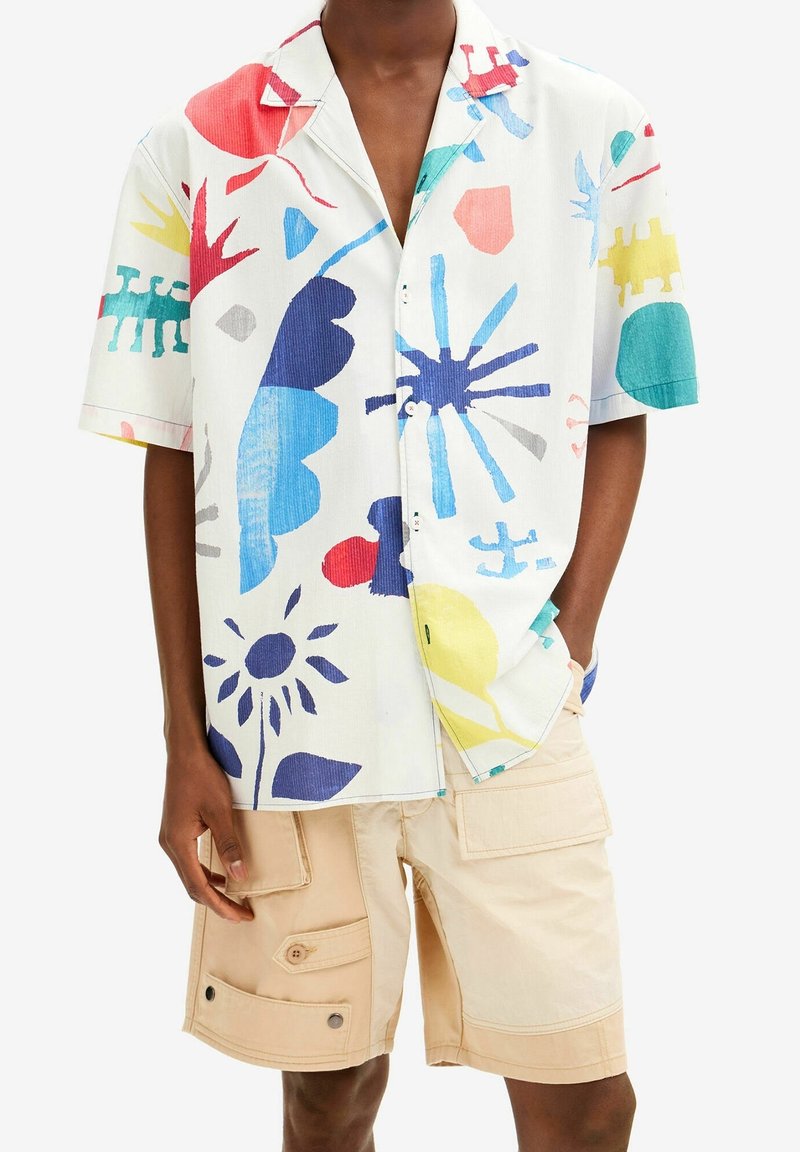 Personne portant une chemise blanche à manches courtes avec des formes abstraites colorées et un short cargo beige avec plusieurs poches.