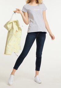 Gray cotton t-shirt with "Moin" text, paired with dark blue skinny jeans and white sneakers. Holding a yellow floral-patterned jacket.