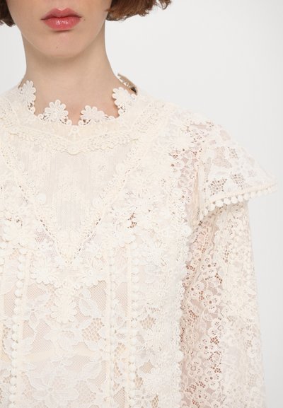 Spitzenbluse mit floralen Mustern in Creme, hohem Kragen mit filigranen Details und strukturierten Oberflächen. Leichte, luftige Stoffzusammensetzung.