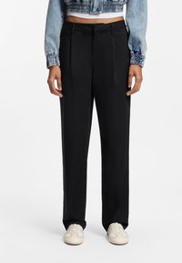 Μαύρο παντελόνι με φαρδιά μπατζάκια, με λεία υφή και πιέτες μπροστά. Συνδυάζεται με κοντό τζάκετ από τζην ύφασμα και ανοιχτόχρωμα αθλητικά παπούτσια.