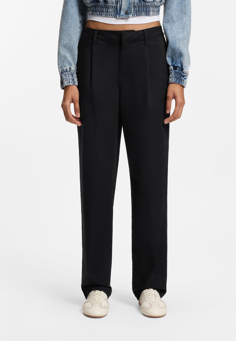 Μαύρο παντελόνι με φαρδιά μπατζάκια, με λεία υφή και πιέτες μπροστά. Συνδυάζεται με κοντό τζάκετ από τζην ύφασμα και ανοιχτόχρωμα αθλητικά παπούτσια.