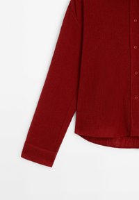 Chemise rouge texturée à manches longues, avec des boutons à l'avant et un ourlet incurvé. Réalisée en tissu léger avec un motif froissé subtil.