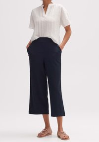 Bílé krátké tričko s měkkou texturou, spárované s námořnicky modrými zkrácenými kalhotami a plochými sandály s pásky.