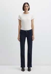 White ribbed short-sleeve top paired with dark blue straight-leg jeans. Jeans have front pockets and subtle stitching details. Black pointed boots.