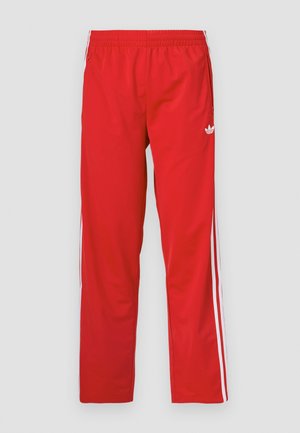 Red track pants made of lightweight fabric with an elastic waistband and white stripes down the sides. Features a small logo near the hip.