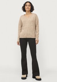 Beige gebreide trui met V-hals en lange mouwen, gecombineerd met zwarte flared broeken en zware beige laarzen. Glad textuur overal.