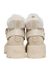 Bottes à plateforme beiges avec semelles à crampons épais, estampillées "Buffalo" sur le talon et la sangle, dotées de cols en shearling duveteux et de languettes de traction à l'arrière.