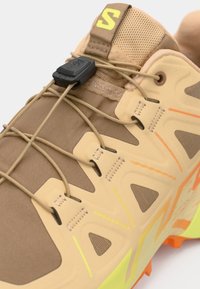 Αθλητικό παπούτσι ταμπά με υφή στην επιφάνεια, ενσωματωμένο σύστημα κορδονιών και ζωντανές πορτοκαλί και κίτρινες λεπτομέρειες, με ανθεκτική σόλα.