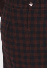 Tessuto a quadri bordeaux e navy con una finitura texture, caratterizzato da un bottone e dettagli con pieghe in vita.