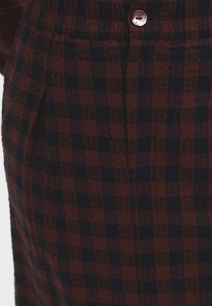 Tissu à motif carreaux bordeaux et marine avec une finition texturée, présentant un détail de bouton et de plis à la taille.