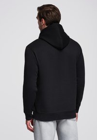 Černá mikina s kapucí, dlouhými rukávy a klokaní kapsou, s texturovanou tkaninou a uvolněným střihem.