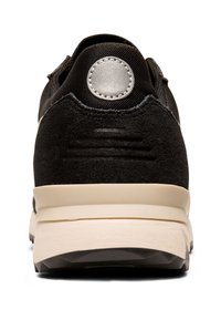 Baskets noires avec un dessus en suède lisse et texturé. Présente un accent argenté rond sur le talon et une semelle beige avec un motif de semelle.