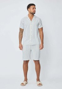 Chemise à manches courtes, boutonnée, et short assorti en rayures verticales bleu clair et blanches, fabriqués en tissu léger, avec une coupe décontractée.