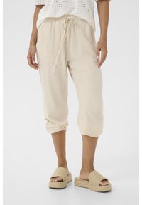 Pantaloni cropped in lino beige con vita elastica e dettaglio con cordoncino, dotati di risvolti e abbinati a sandali beige con texture.
