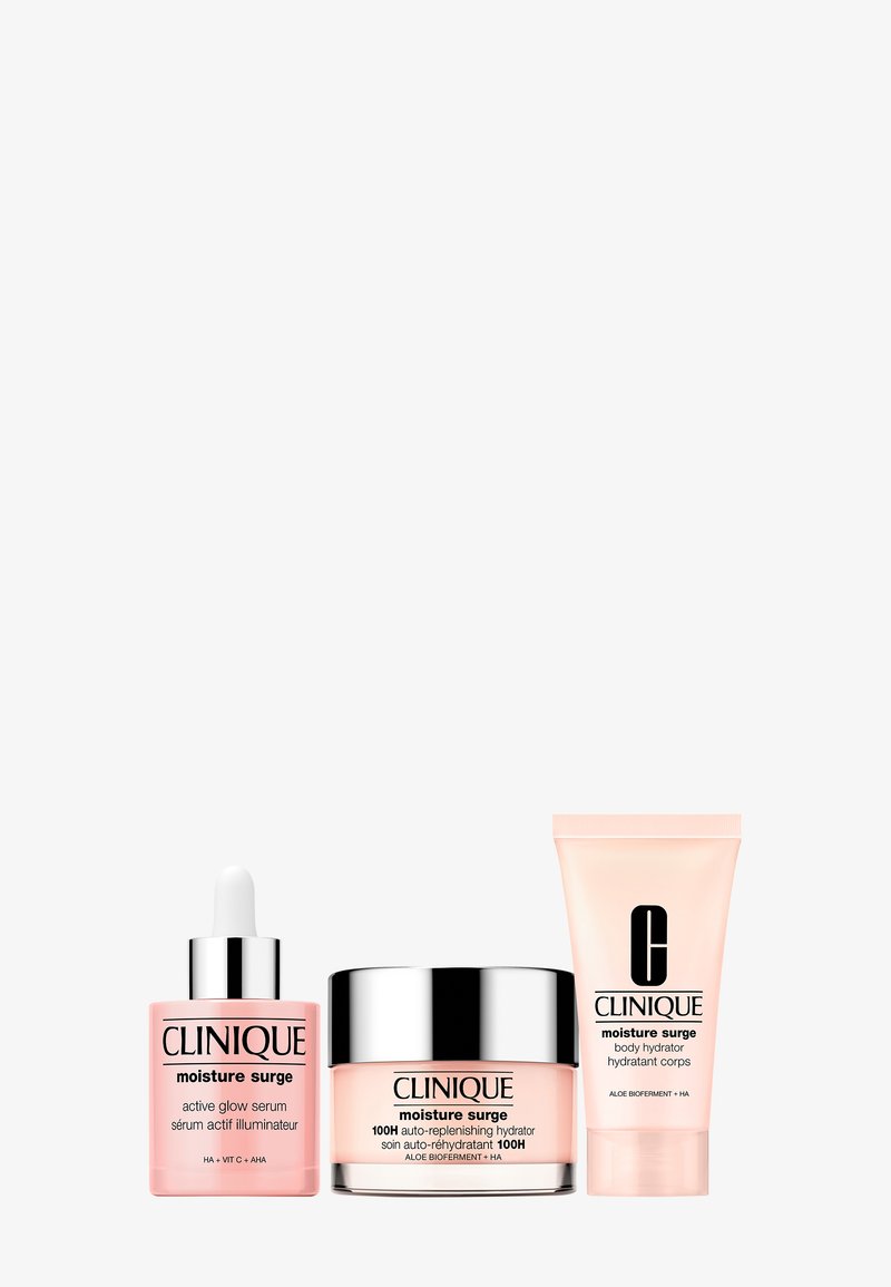 Set Clinique Moisture Surge con cuentagotas de suero de brillo activo, tarro hidrantante autorreponible de 100 horas y tubo hidratante corporal sobre fondo blanco.