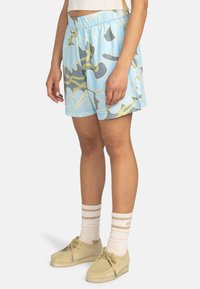 Shorts bleu clair avec un motif floral et abstrait en jaune et gris, dotés d'une taille élastique et de poches latérales.