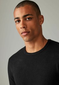Sort strikket sweater, rund hals, glat tekstur, tætsiddende design. Minimalistisk stil uden synlige mønstre eller aksenter.