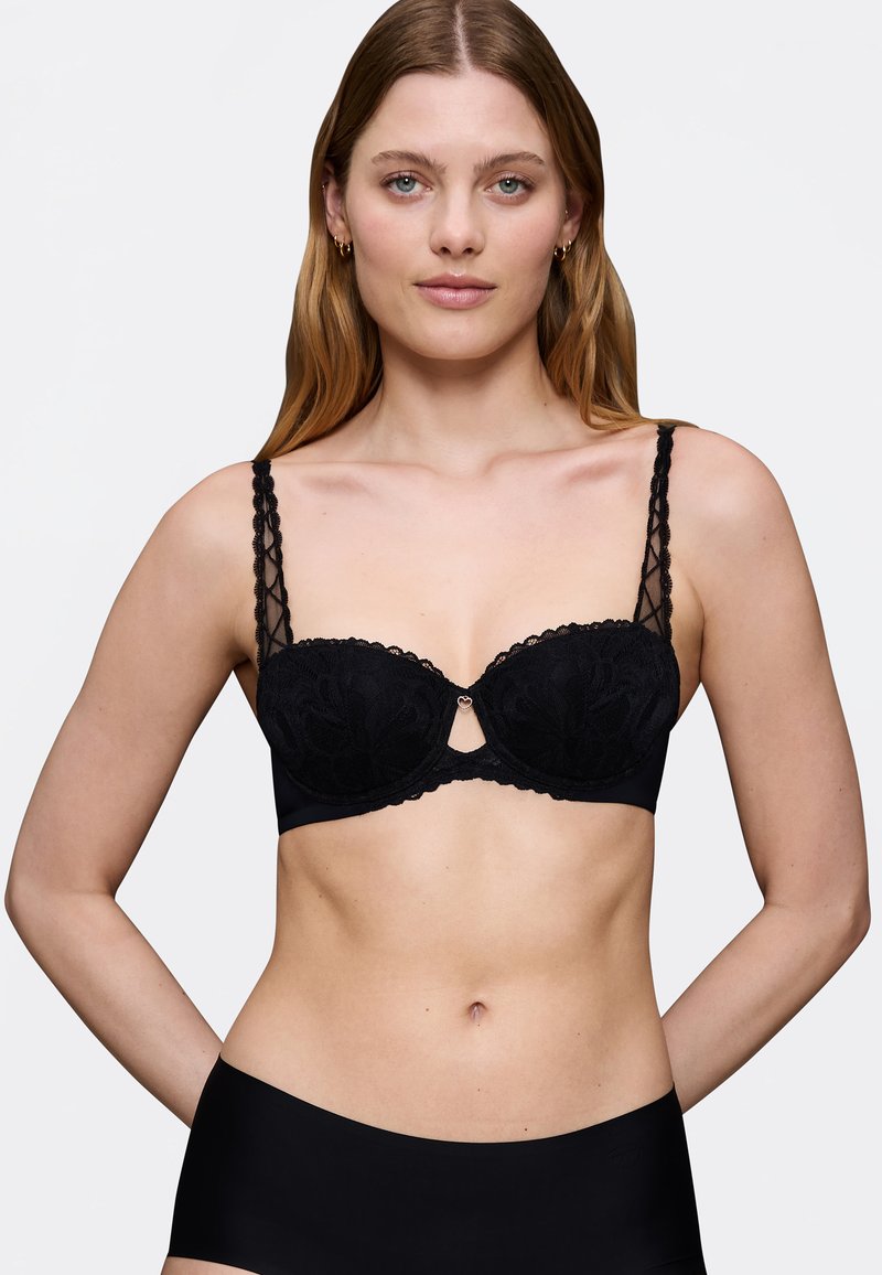 Reggiseno in pizzo nero con stecche, fantasie floreali, bordi scallop e dettaglio a chiave sul davanti. Spalline nere semplici con un design testurizzato.