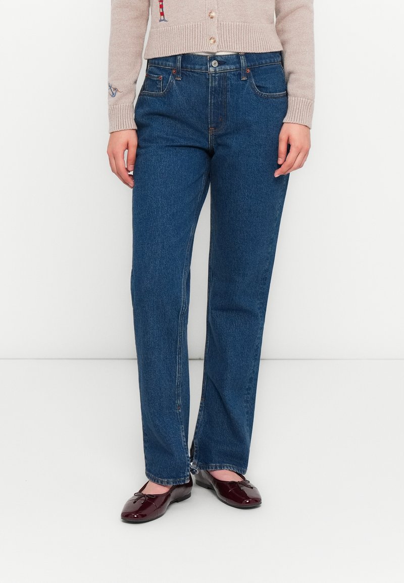 Blauwe high-waisted jeans met een rechte pijp, van denim materiaal, vijf zakken en subtiele stikselaccenten. Gekleed met bordeauxkleurige ballerina's.