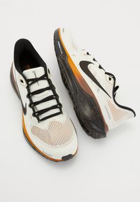 White athletic shoes with black accents, textured mesh upper, synthetic overlays, and orange detailing on the midsole and outsole.