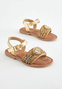 Goldfarbene Metallic-Sandalen mit einem strukturierten, perlenbesetzten Riemen mit floralen Design, einem verstellbaren Knöchelriemen und einer braunen, kunstledersohle.