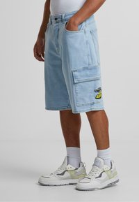 Lyse blå denim cargo-shorts med sidelommer og broderte detaljer. Pair med hvite og grå joggesko og ribbede sokker.
