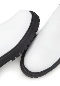 Witte leren enkellaarsjes met een stevige zwarte rubberen zool. Ronde neusvorm en een gladde textuur met zichtbare stiksels.