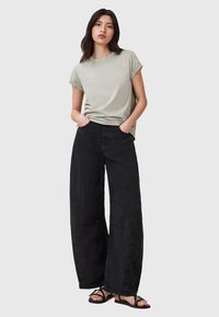 T-shirt grigio chiaro a maniche corte abbinato a pantaloni neri a gamba larga. Sandali con cinturini sottili. L'outfit ha una vestibilità rilassata e informale.