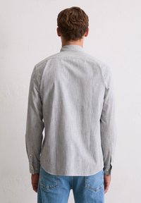 Szara pasiasta koszula z długim rękawem, standardowym kołnierzykiem, mankietami na guziki i prostym dołem, zestawiona z jasnoniebieskimi dżinsami.