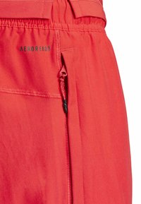 Red activewear shorts with a smooth texture, featuring an elastic waistband, drawstring, and a zippered pocket with black accents.