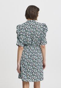 Rochie florală cu mâneci bufantă, având un fond negru și mici modele florale roz, albastre și verzi. De lungime medie, cu talie încinsă.