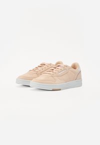 Lyserøde ruskinds sneakers med en hvid gummisål, der har en rund tå, perforerede detaljer og en lille hvid accent på hælen.