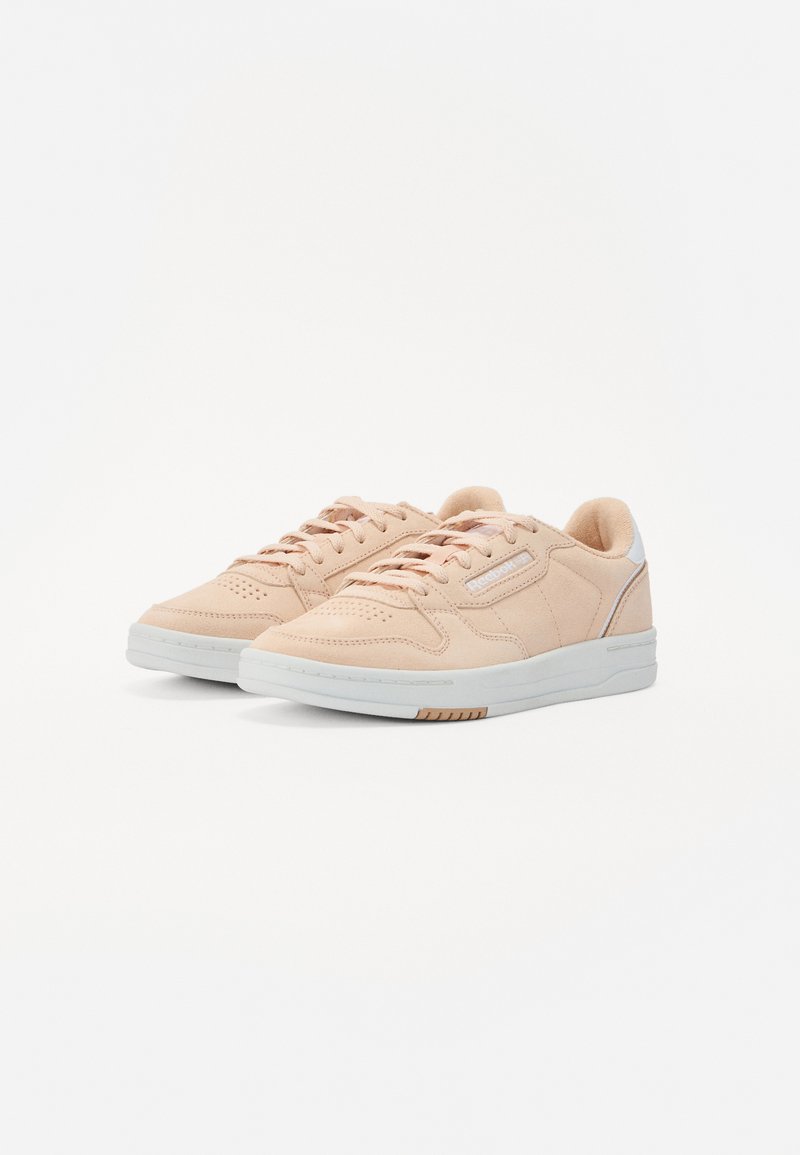 Zapatillas de ante rosa claro con suela de goma blanca, que presentan una punta redondeada, detalles perforados y un pequeño acento blanco en el talón.