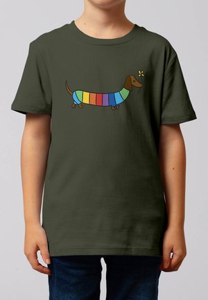 Kind draagt een donkergroen shirt met een cartoon teckel in regenboogkleuren en een kleine gele vlinder vlakbij zijn neus.