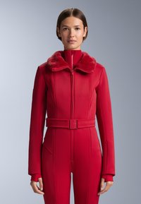 Piros, cipzárral záródó dzseki műszőrmés gallérral, bordázott textúrával és testhez simuló szabással. Derékrészen övvel, az ujjak végén pedig hüvelykujj nyílásokkal.