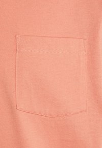 Gros plan sur une poche en tissu couleur pêche avec des coutures visibles sur un vêtement.