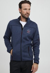 Navy Fleece-Jacke mit Reißverschluss, langen Ärmeln, seitlichen und Brusttaschen, kontrastierendem schwarzen Reißverschluss und roten Akzenten, strukturiertem Stoff.