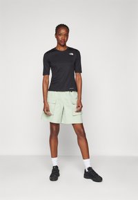 Svart kortärmad skjorta med logotyp och gröna cargoshorts med framfickor. Bärs med vita strumpor och svarta skor.