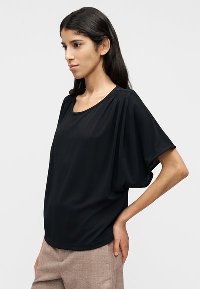 Μαύρο κοντομάνικο τοπ με άνετη εφαρμογή, στρογγυλή λαιμόκοψη και ριγμένη λεπτομέρεια στους ώμους. Λείο ύφασμα με ελαφριά υφή.
