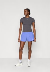 Γκρι αθλητική κοντομάνικη μπλούζα Nike με λογότυπο, σε συνδυασμό με ανοιχτό μπλε σορτς. Το σύνολο διαθέτει εφαρμοστή γραμμή και ελαφρύ υλικό.