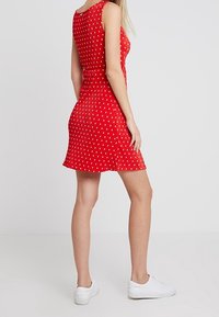 Rotes ärmelloses Kleid mit weißen Punkten, A-Linie, strukturierten Stoff, mittlere Oberschenkel-Länge, kombiniert mit weißen Sneakers.